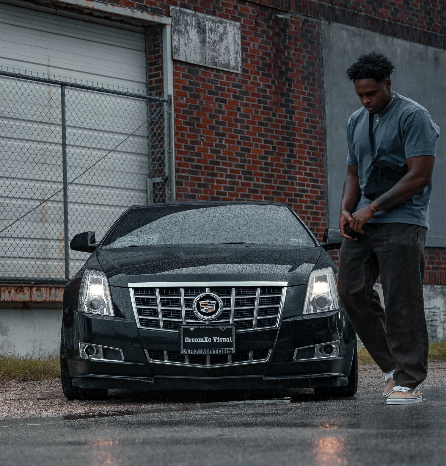 Man standing next to a black Cadillac car in front of a brick building.